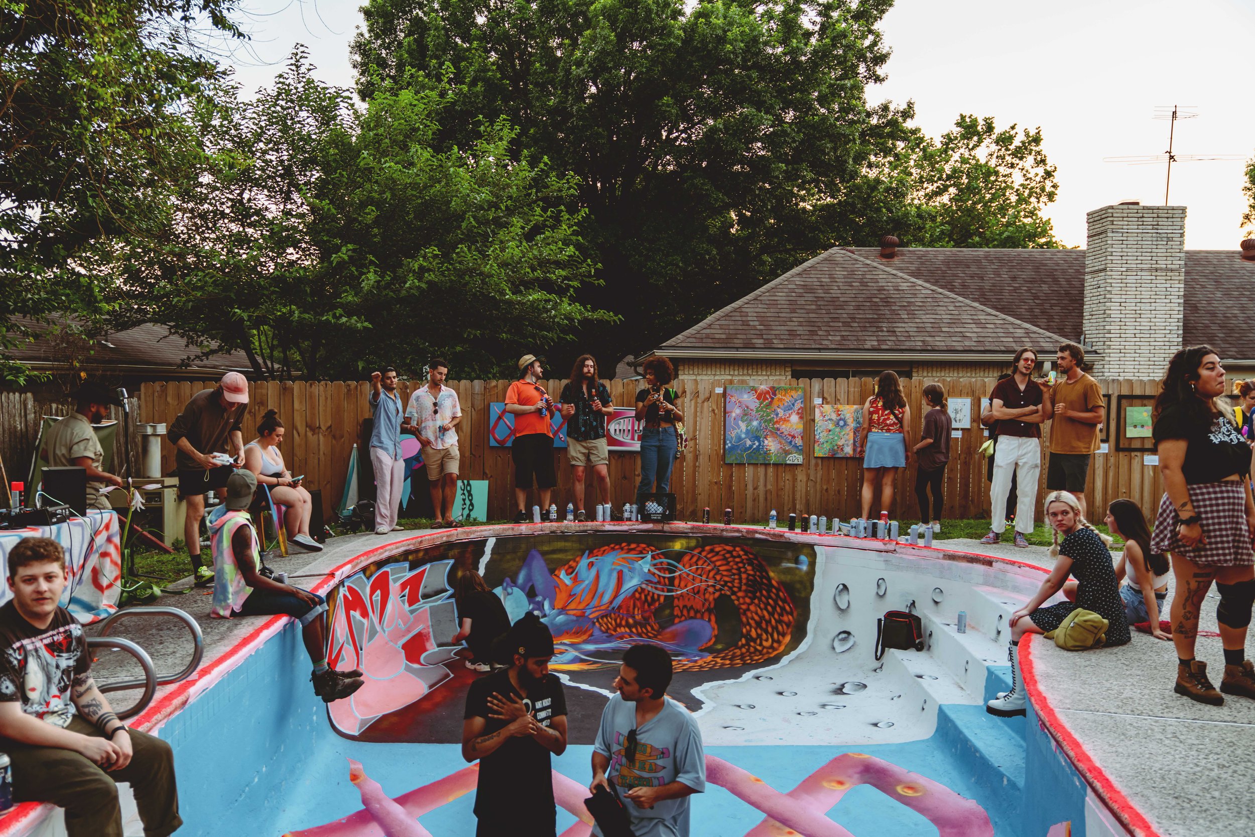 Young people talk at a party in a backyard inside of an empty pool painted in a variety of murals and patterns.
