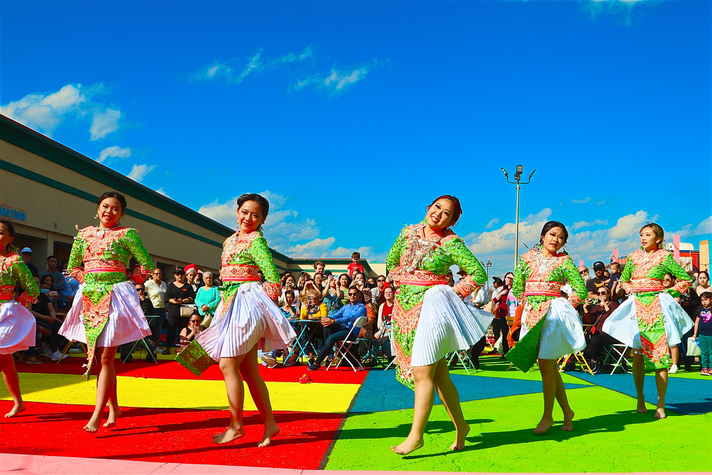 Women in flowy dresses perform on a multicolored stage in front of a crowd at the Tulsa Global District in Tulsa, oklahoma.
