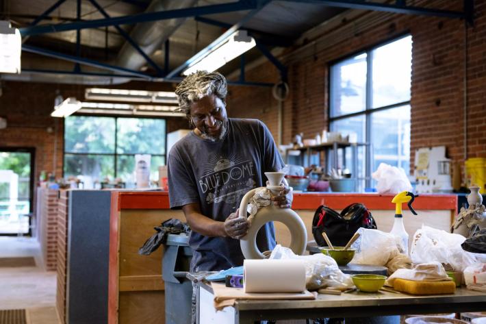 Man attaching handle on clay vase at pottery studio.