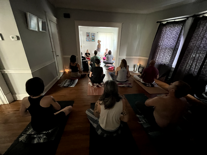 A group of women take a yoga class inside of a dimly lit home.